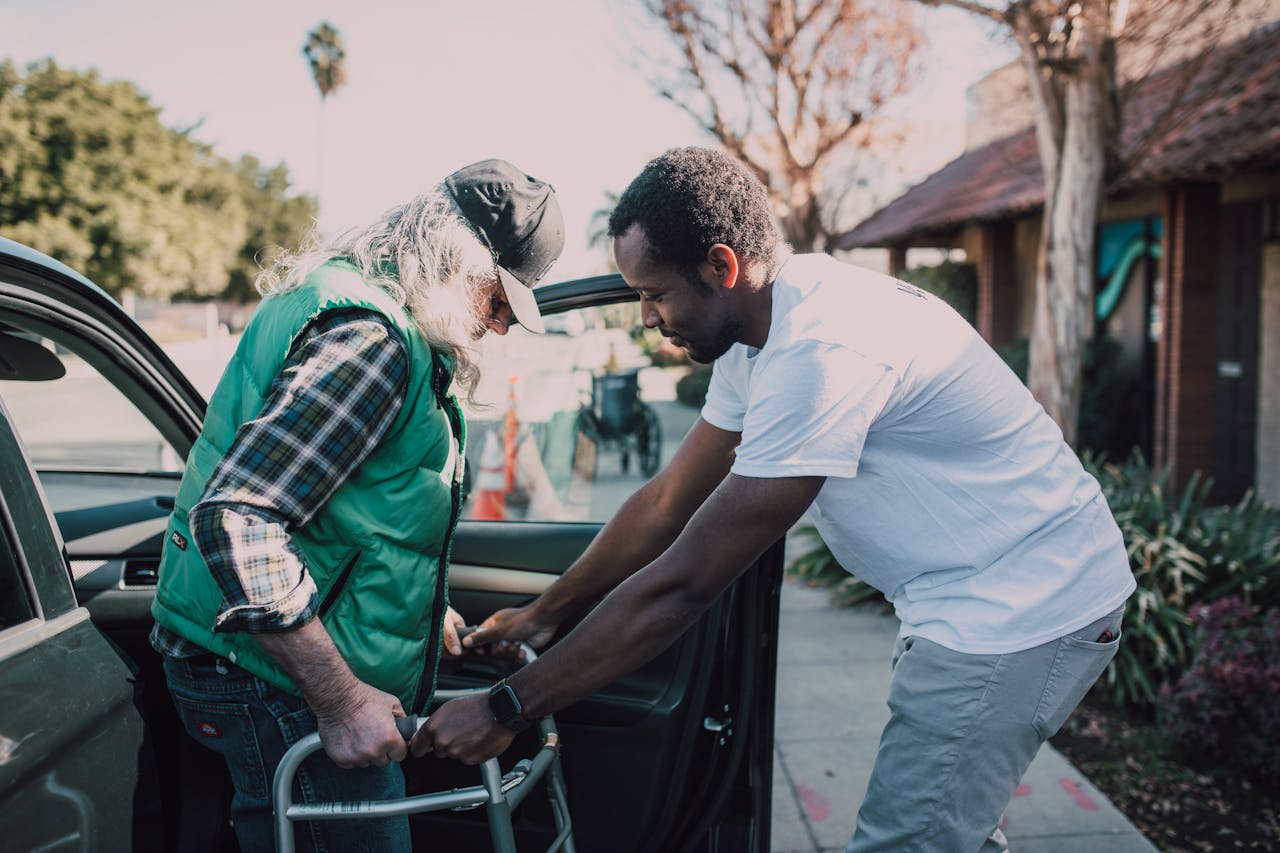 Young volunteer helping senior man with walker near a parked car, symbolizing care and support.